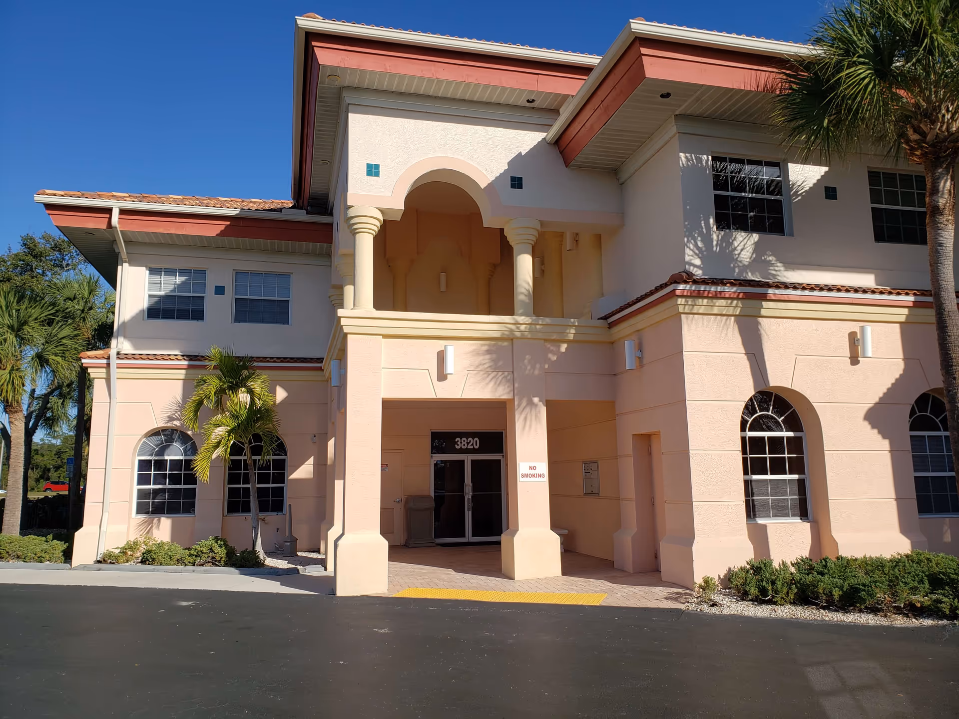 Front view of a peach-colored two-story building with archway entrance and palm trees.