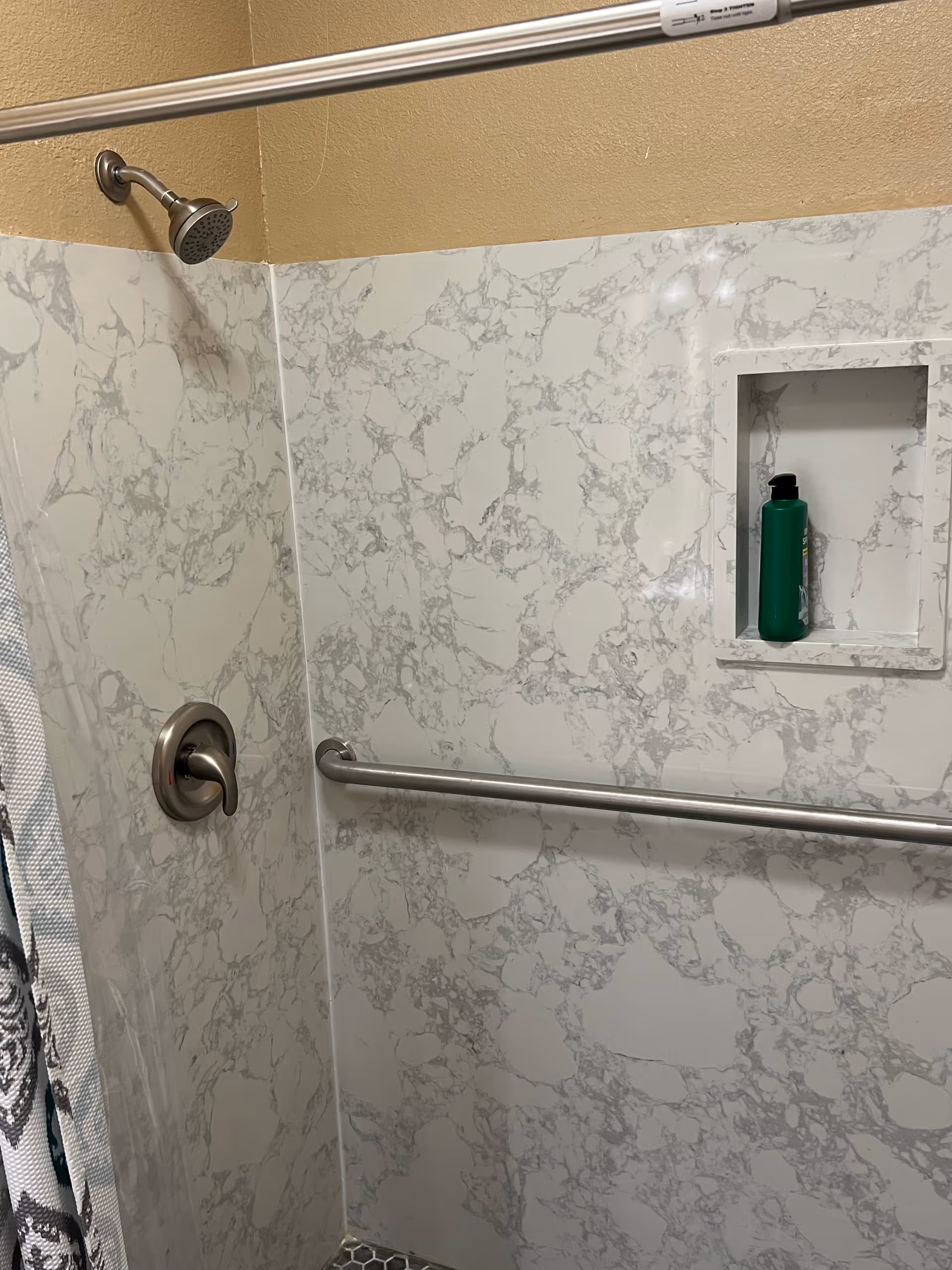Marble shower walls with a built-in niche, showerhead, and grab bar.