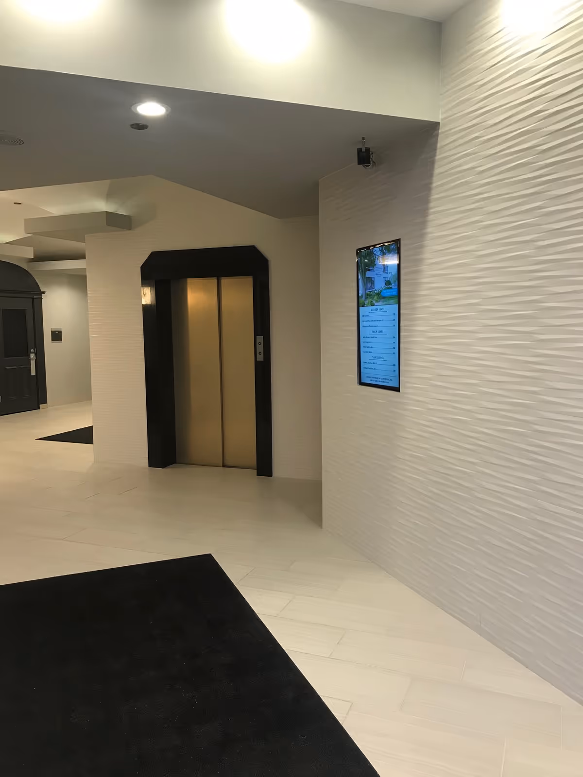 Modern white lobby with an elevator, textured wall, and wall-mounted digital display