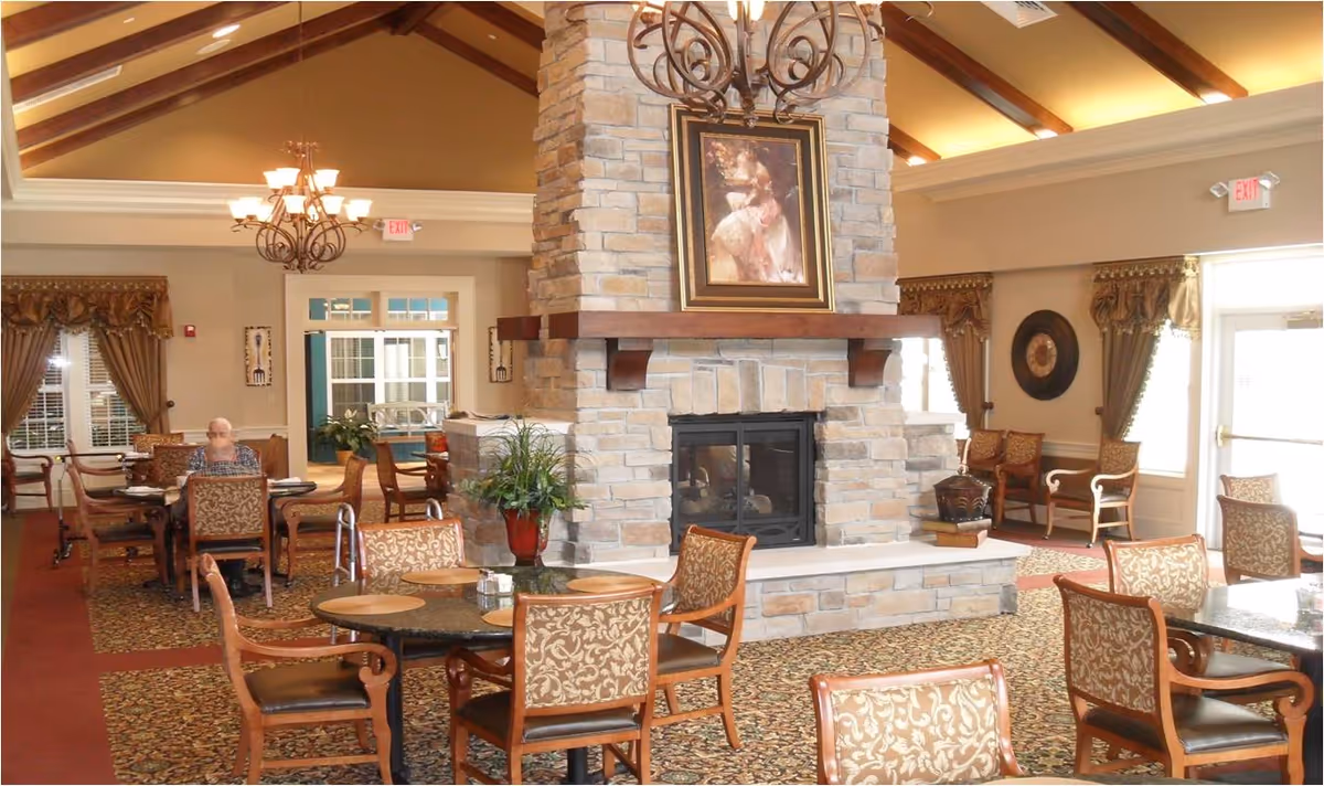 A spacious senior living lounge with a stone fireplace, chandeliers, and seating.