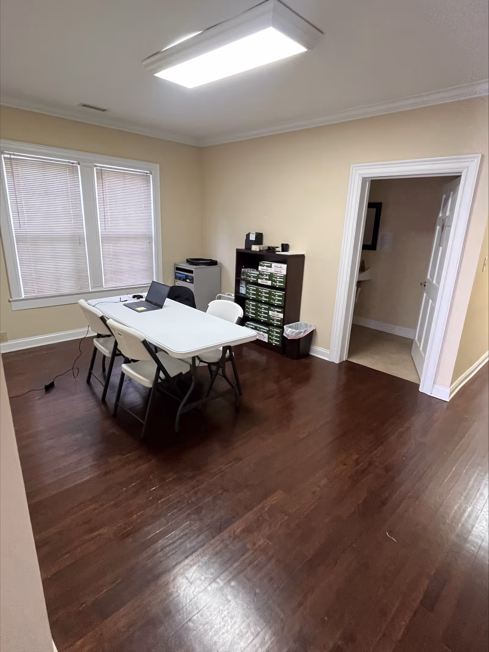 A small meeting room with a white folding table, laptop, chairs, and filing cabinet.