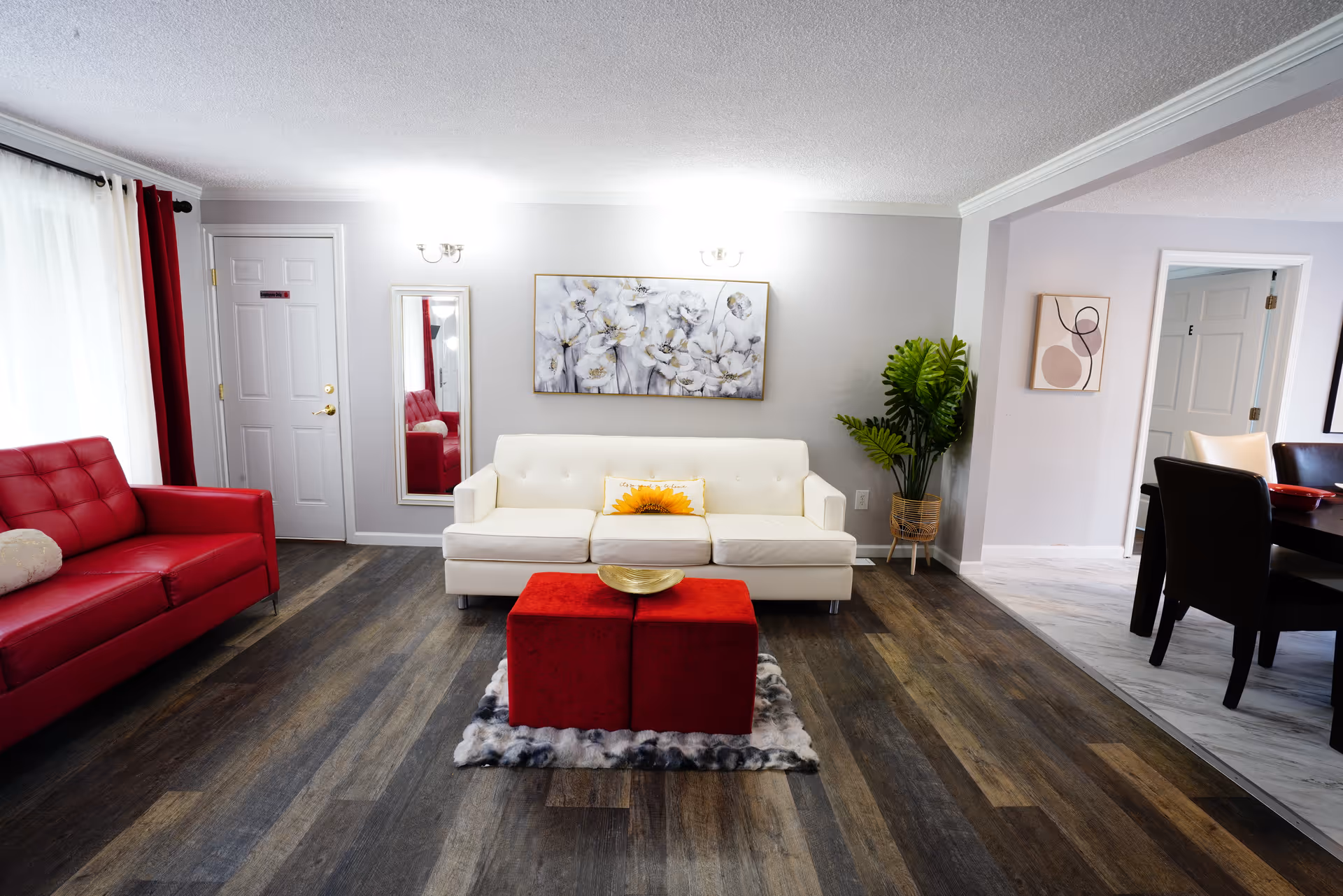 Modern living room in a senior facility with white sofa, red chairs, and dining space nearby.