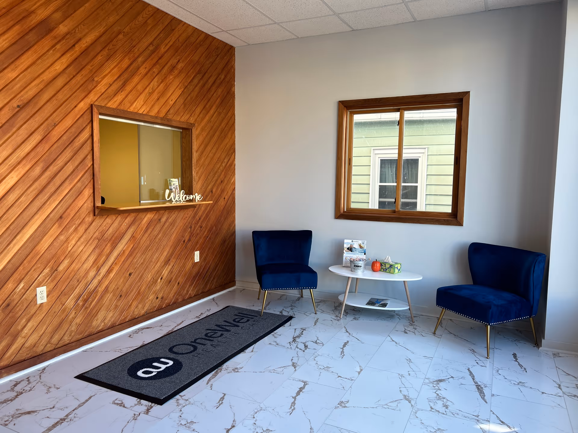 Reception seating area with blue chairs, a white round table, marble floor, and wood-paneled wall.