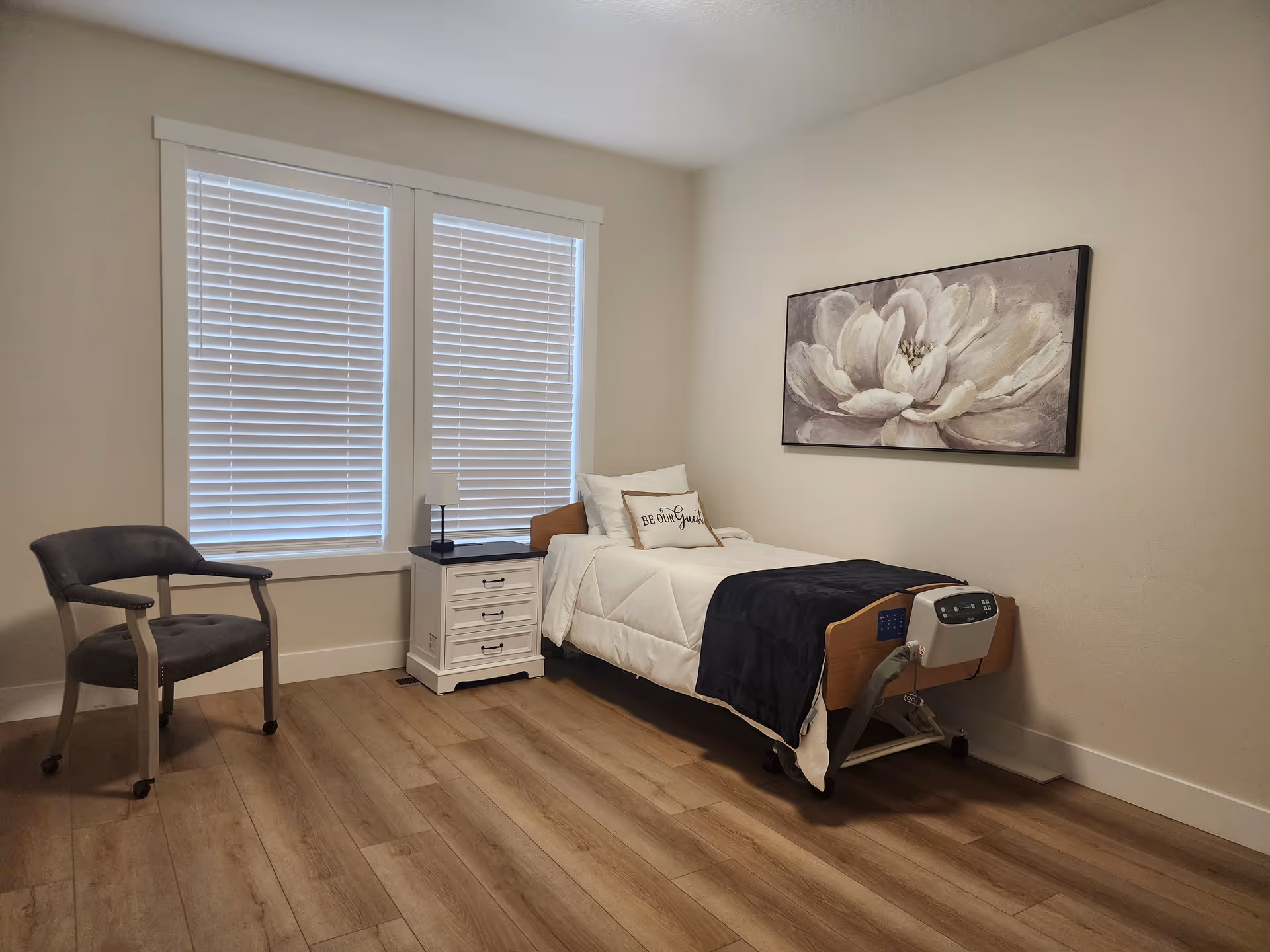 A clean bedroom with a single bed, nightstand, chair, and floral wall art.