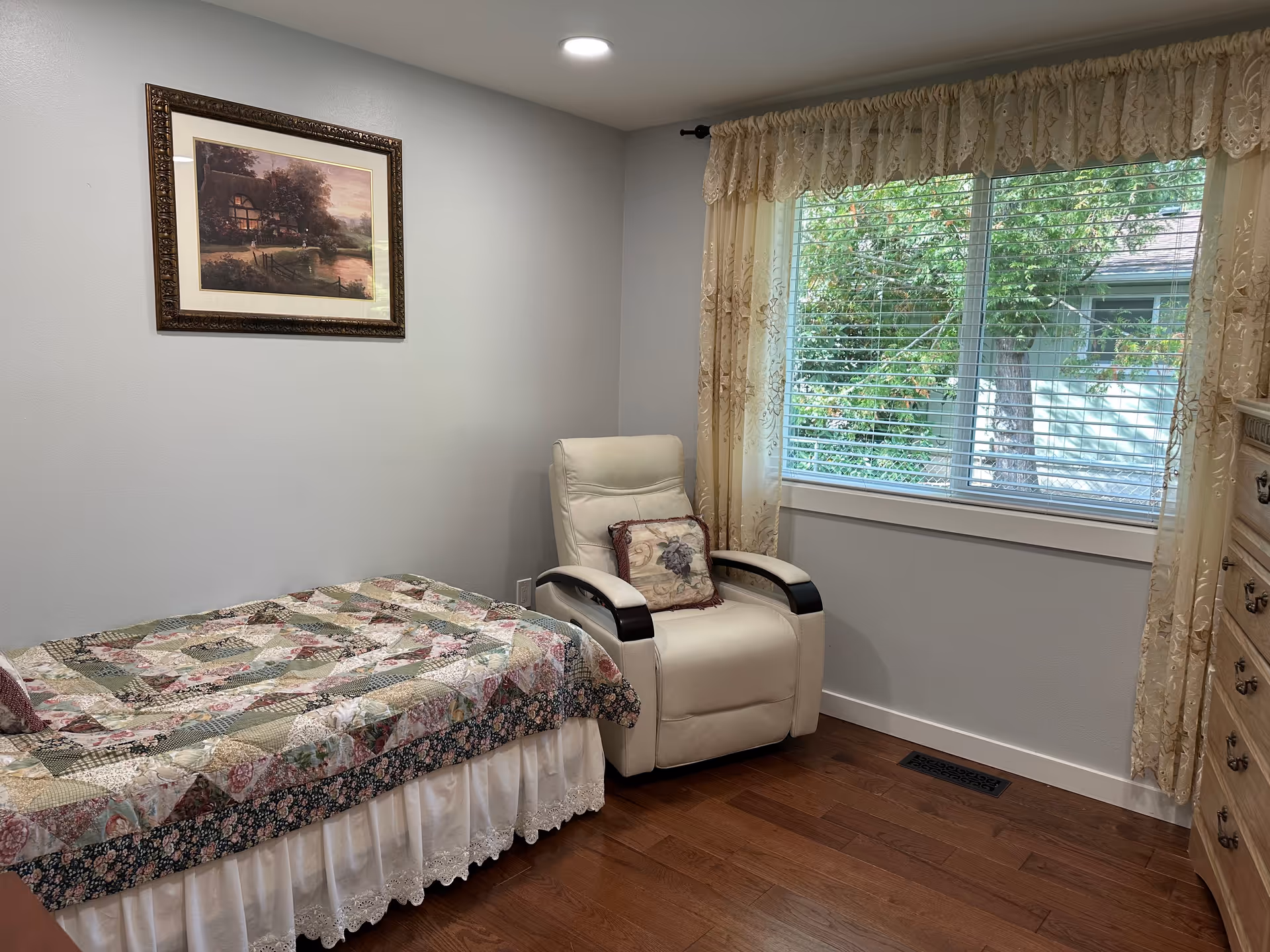 Small bedroom with a patchwork quilt on the bed, a white recliner, and window.