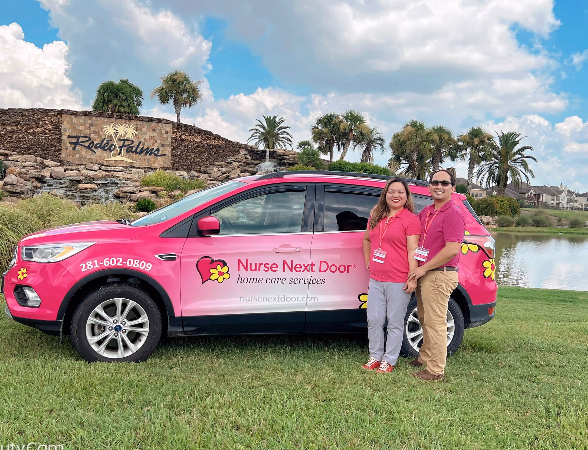 Two smiling caregivers stand beside a pink Nurse Next Door van outdoors.