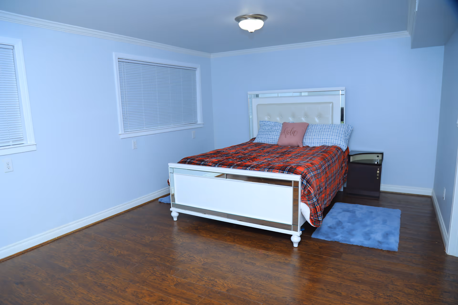 Bright bedroom with metal-framed bed, plaid red blanket, blue walls, and a nightstand.