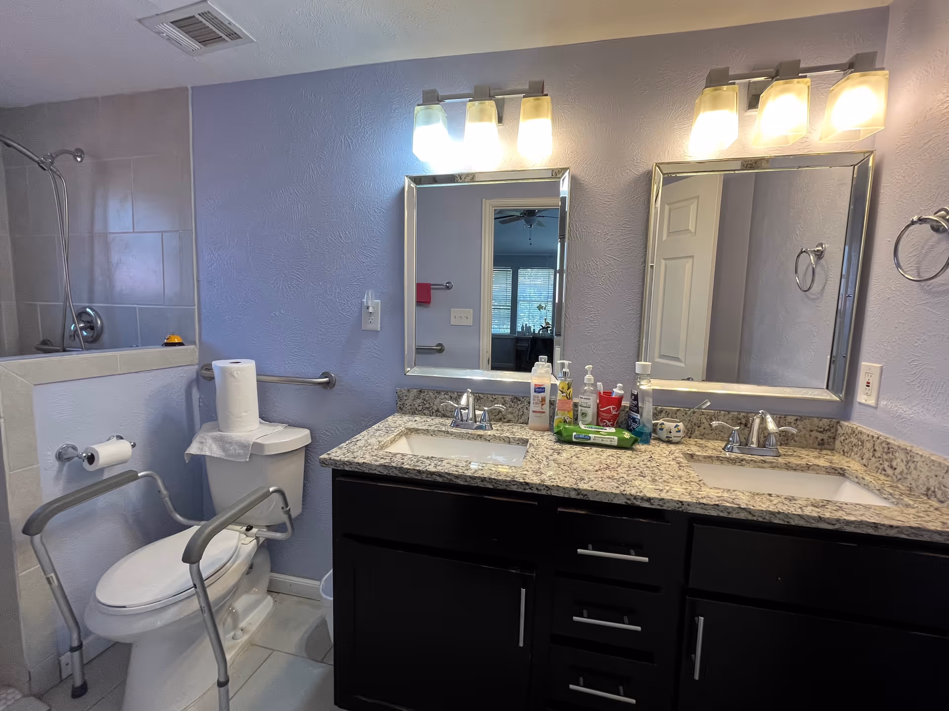 Bathroom with dual sinks, granite counter, large mirrors, and accessible toilet.