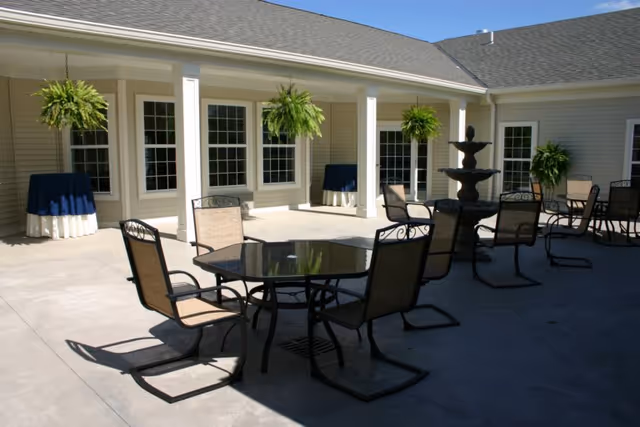 Outdoor courtyard seating with tables, chairs, hanging ferns, and a fountain by a building.