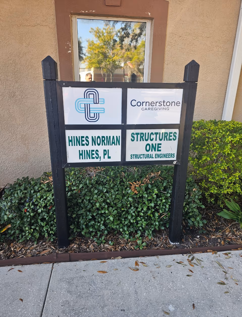 Exterior signboard for Cornerstone Caregiving near shrubs in front of a beige building.