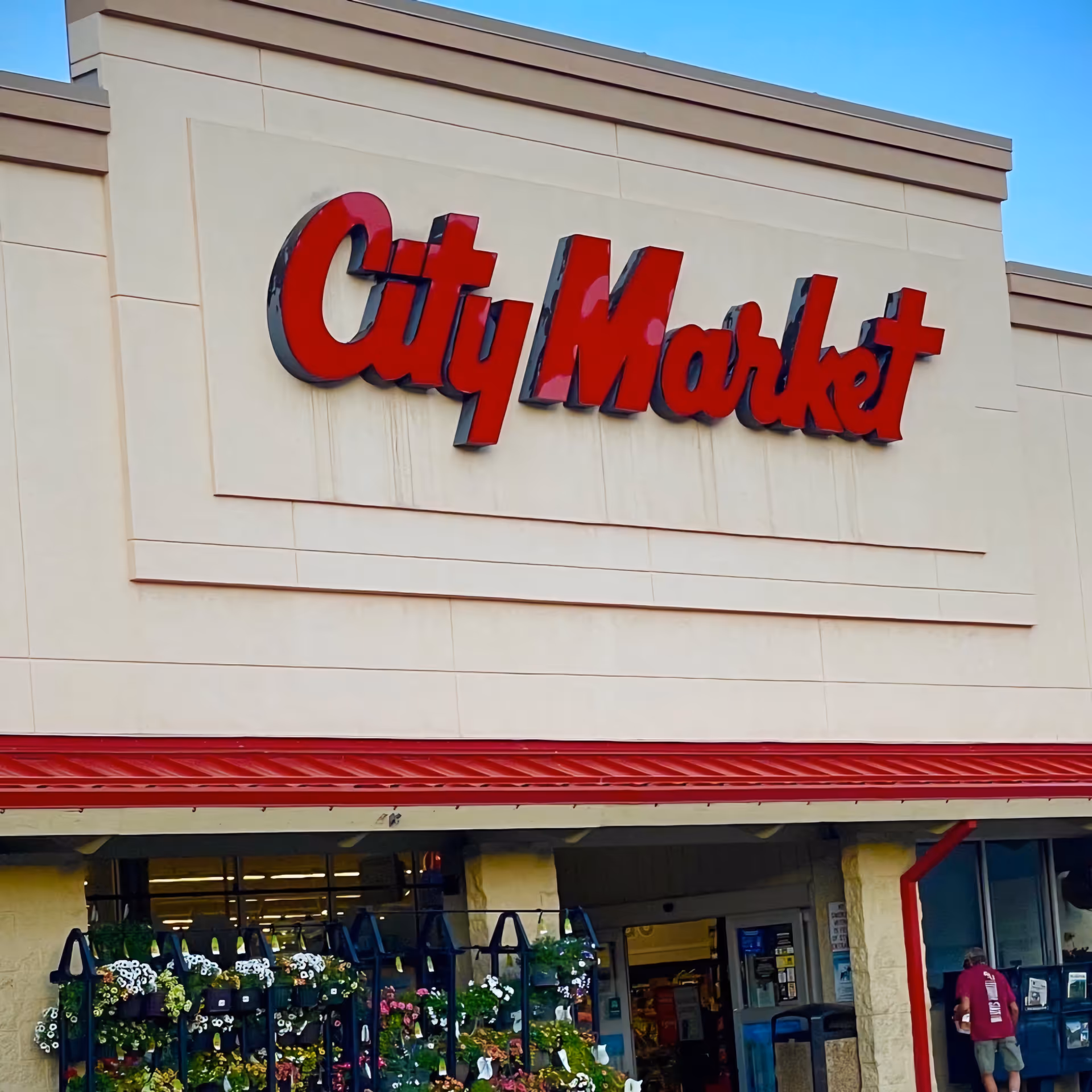 Storefront of City Market Pharmacy with red signage and hanging plants at entrance