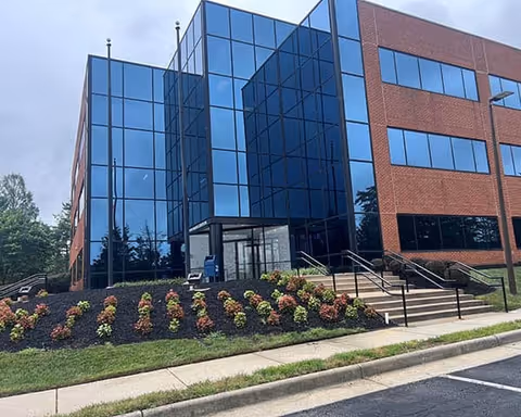 Modern glass-front building exterior with brick facade and landscaped front entrance.