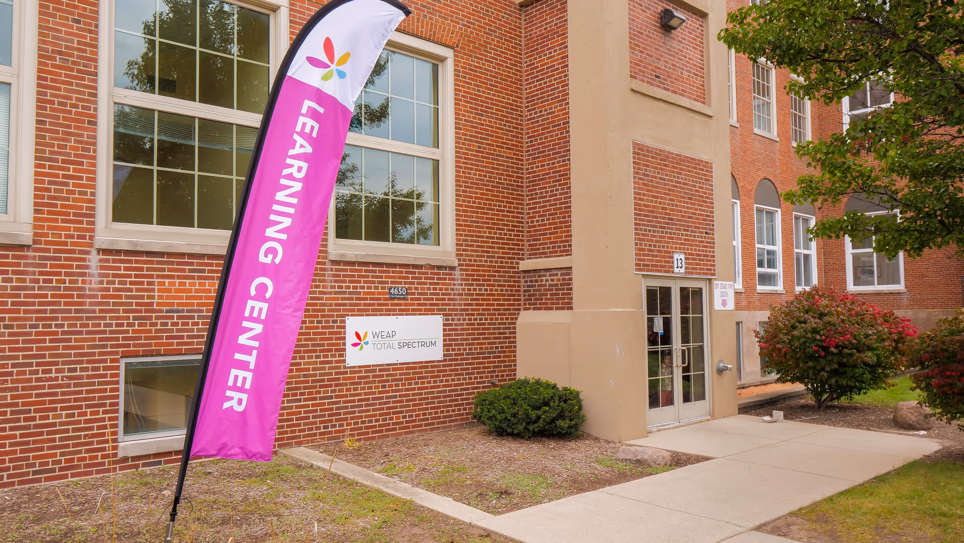 Brick building exterior with a tall pink Learning Center flag near the entrance.