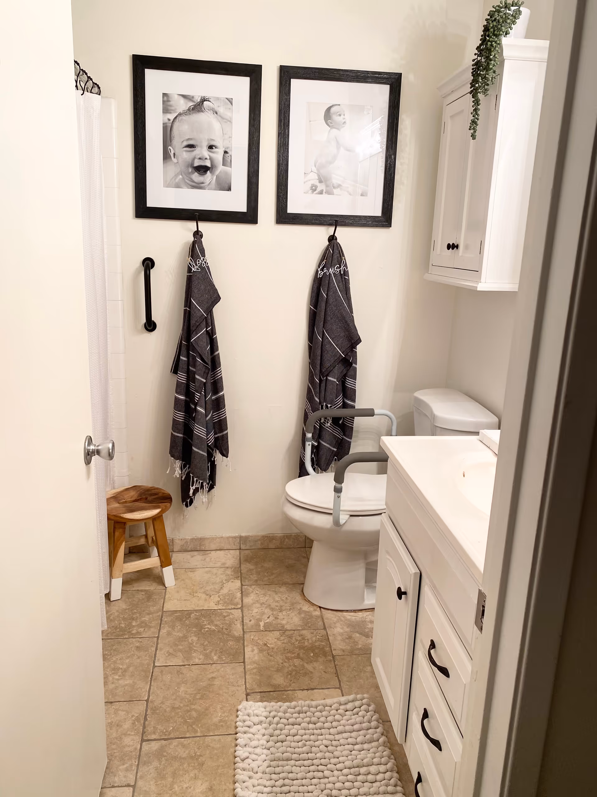 Small bathroom with sink, toilet, grab bar, framed baby photos, towels, and rug.