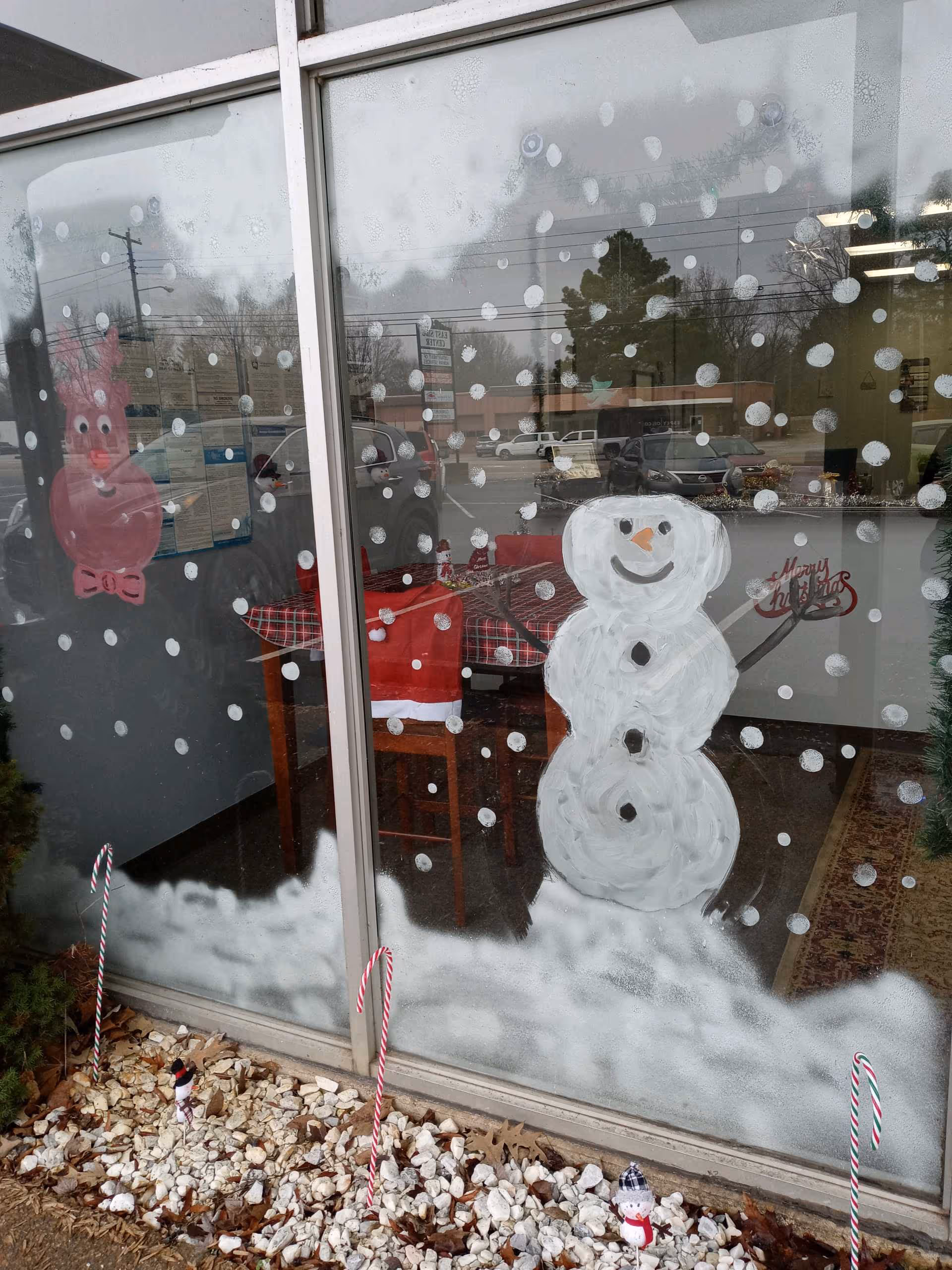 Window decorated with a snowman drawing and snow dots, with holiday candy canes outside.