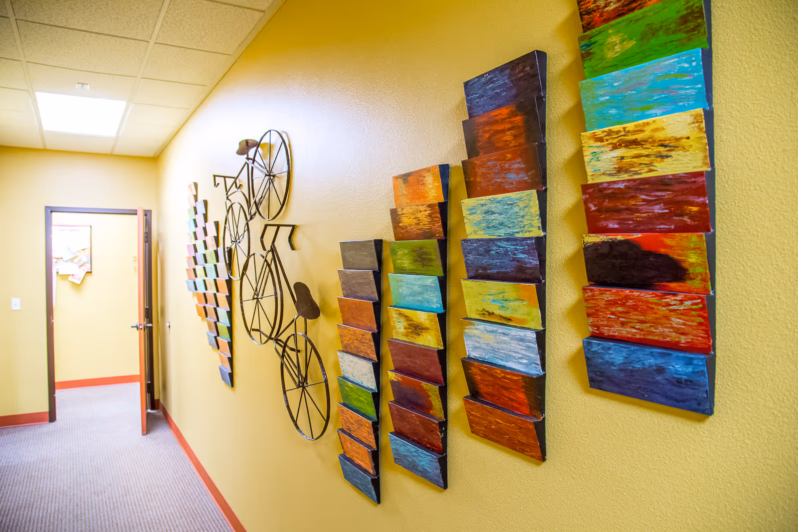 Yellow hallway with colorful wall art and a bicycle sculpture on the wall.