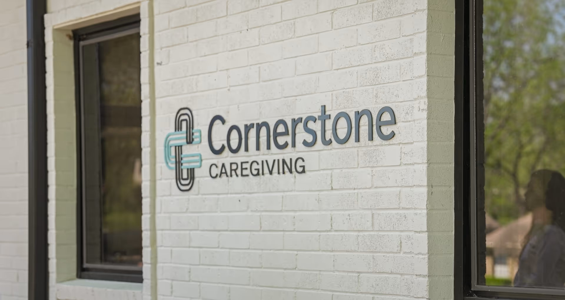 Exterior brick wall with Cornerstone Caregiving sign and a window on the left