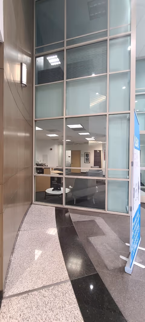 Tall glass partition wall reveals a lobby-like office area through its panes.