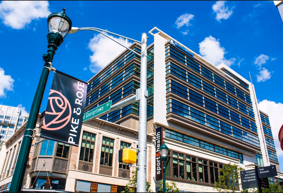 Modern glass-front building on a corner with banners and blue sky.