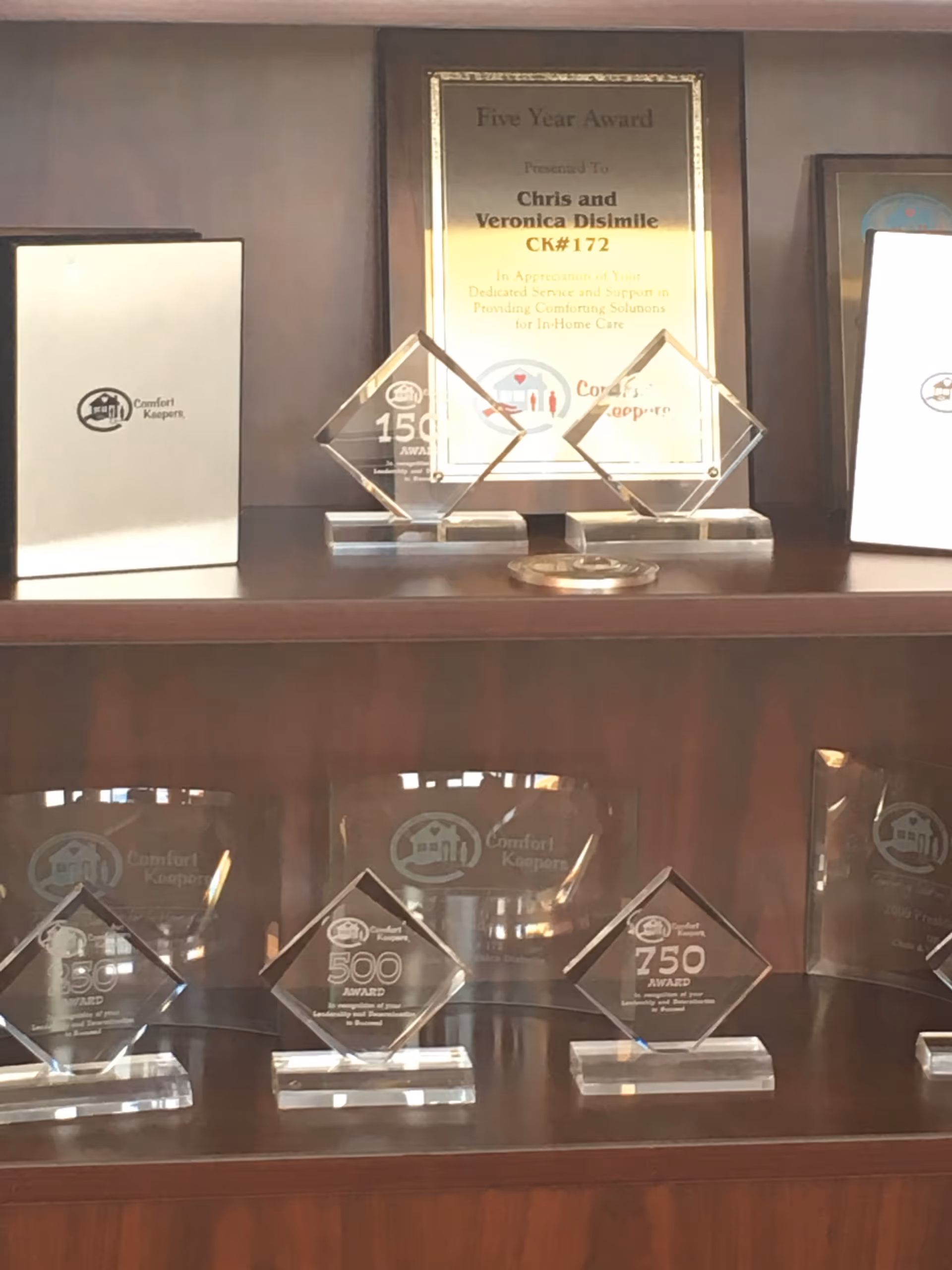 Wooden shelf containing glass awards and plaques with Comfort Keepers logos