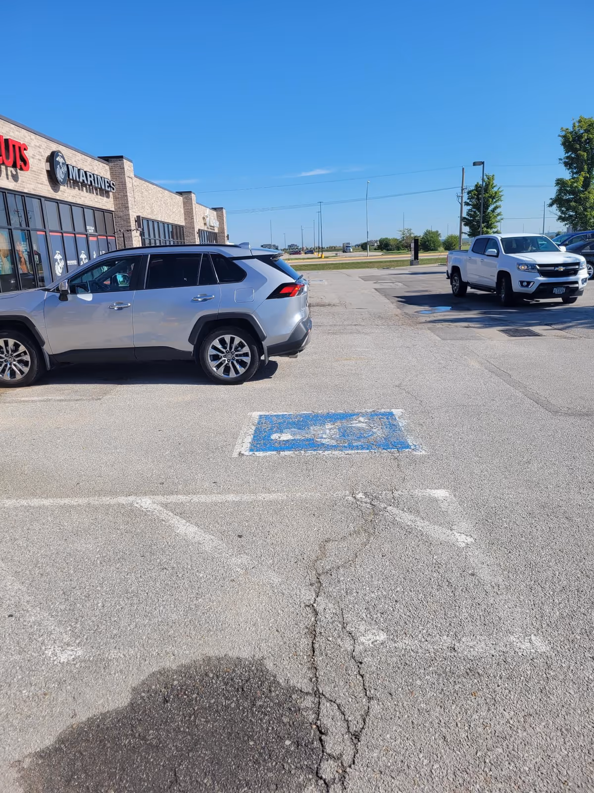 Parking lot in front of a strip mall with cars and storefront windows.
