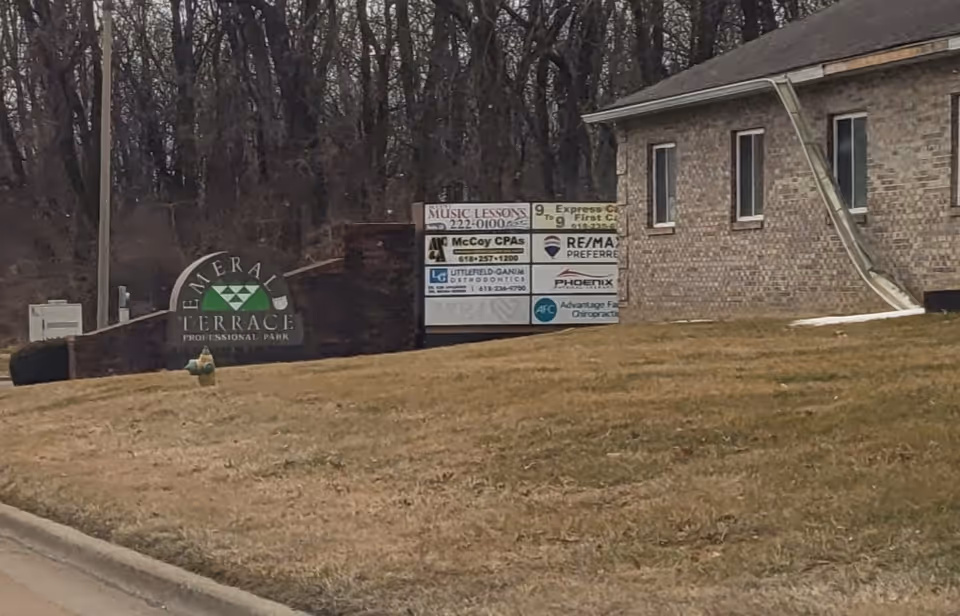 Exterior brick building with a row of signs on a grassy front yard by the road.