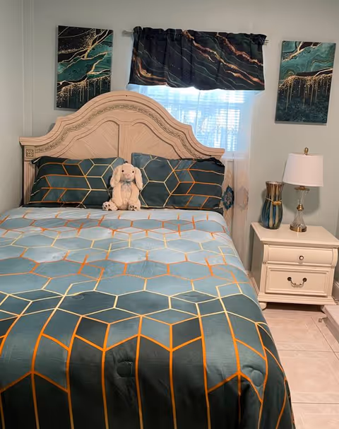 Neatly made bedroom with geometric teal bedding and a plush bunny on the bed.