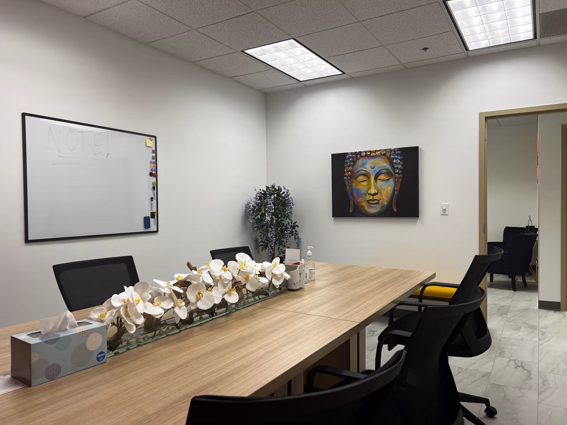 A modern meeting room with a long wooden table, chairs, whiteboard, and wall art.