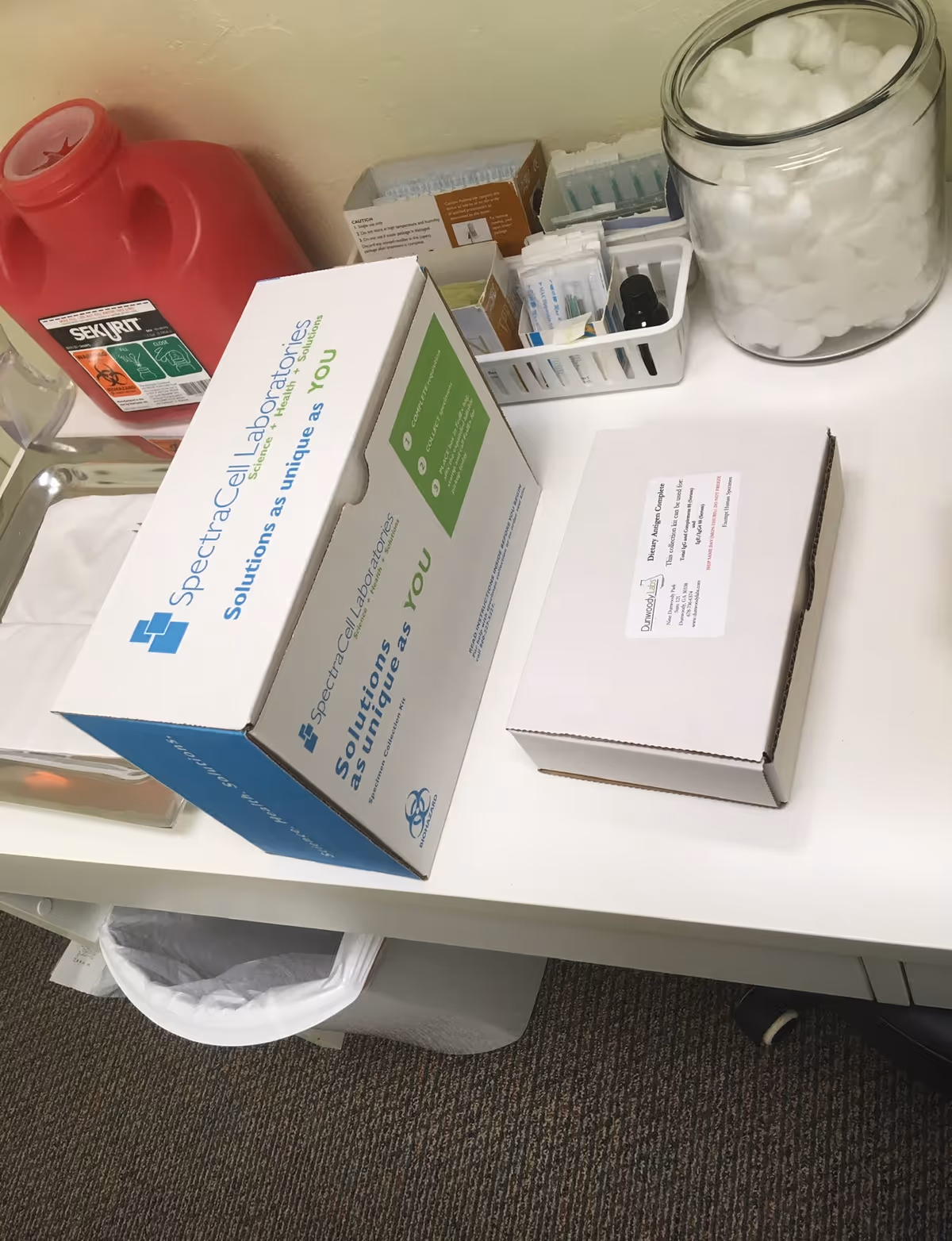 Medical supply desk with boxed testing kits, cotton jar, and storage basket inside clinic.