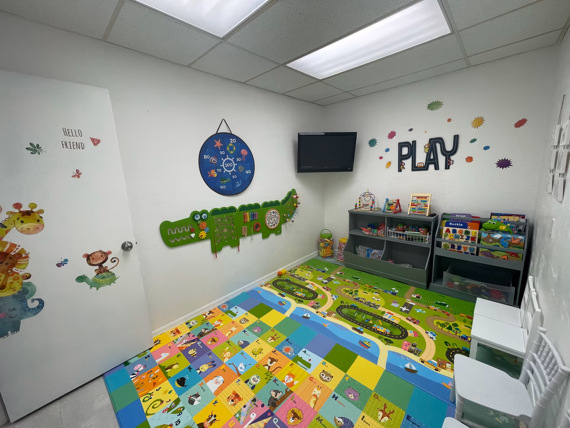 Bright children's playroom with colorful floor mat, toys, and a 'PLAY' wall display.