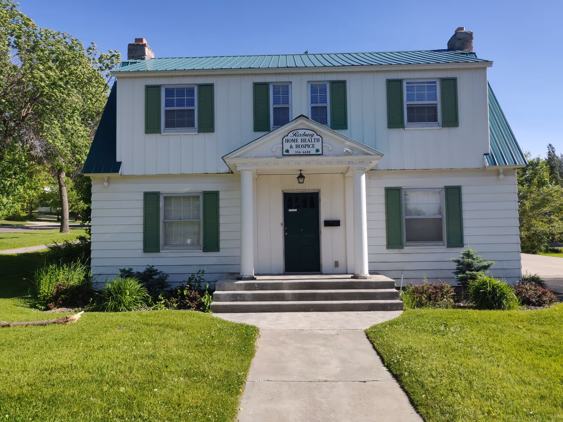 White two-story building with green shutters and a front porch sign reading Home Health and Hospice.