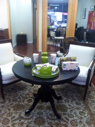 Round black table with green dishware and two white cushioned chairs in lounge with patterned rug
