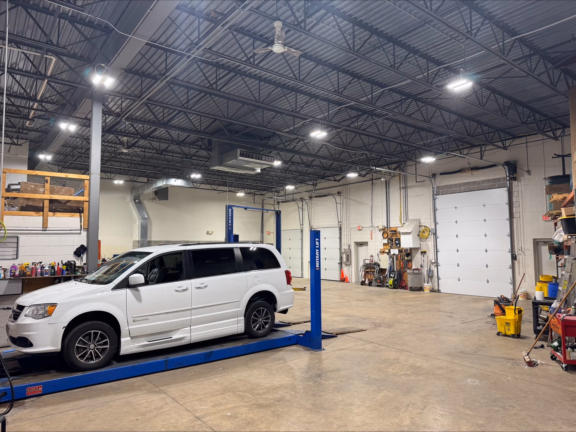 White minivan on a blue car lift inside a large automotive workshop