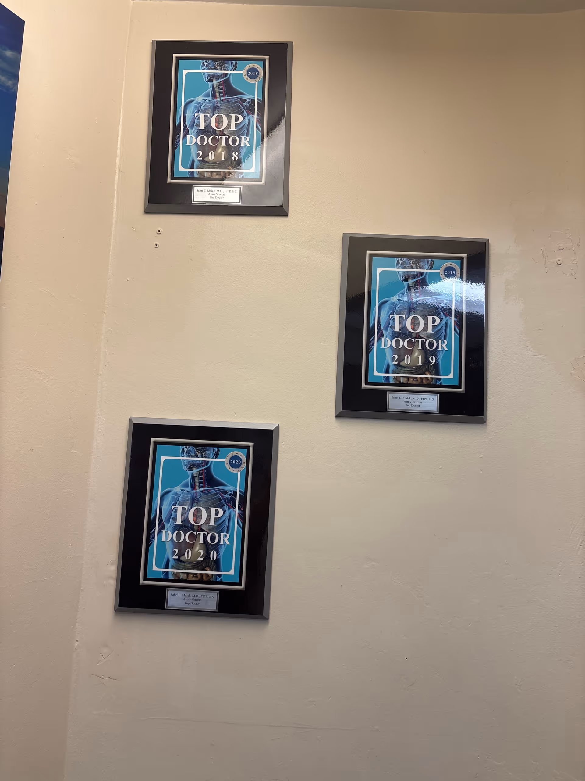 Beige wall with three framed Top Doctor award plaques displayed in a hallway.