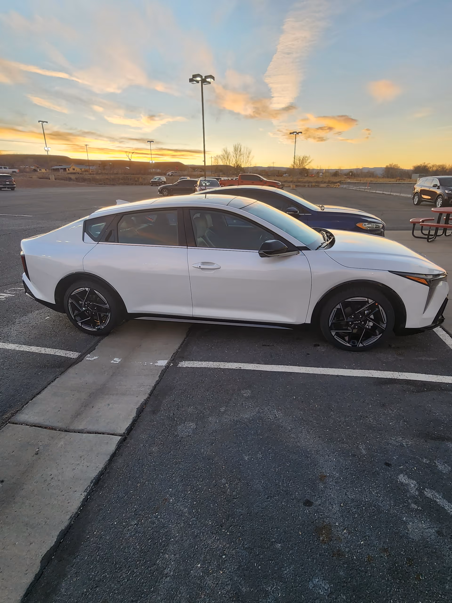 A white sedan parked in a large outdoor parking lot at sunset.