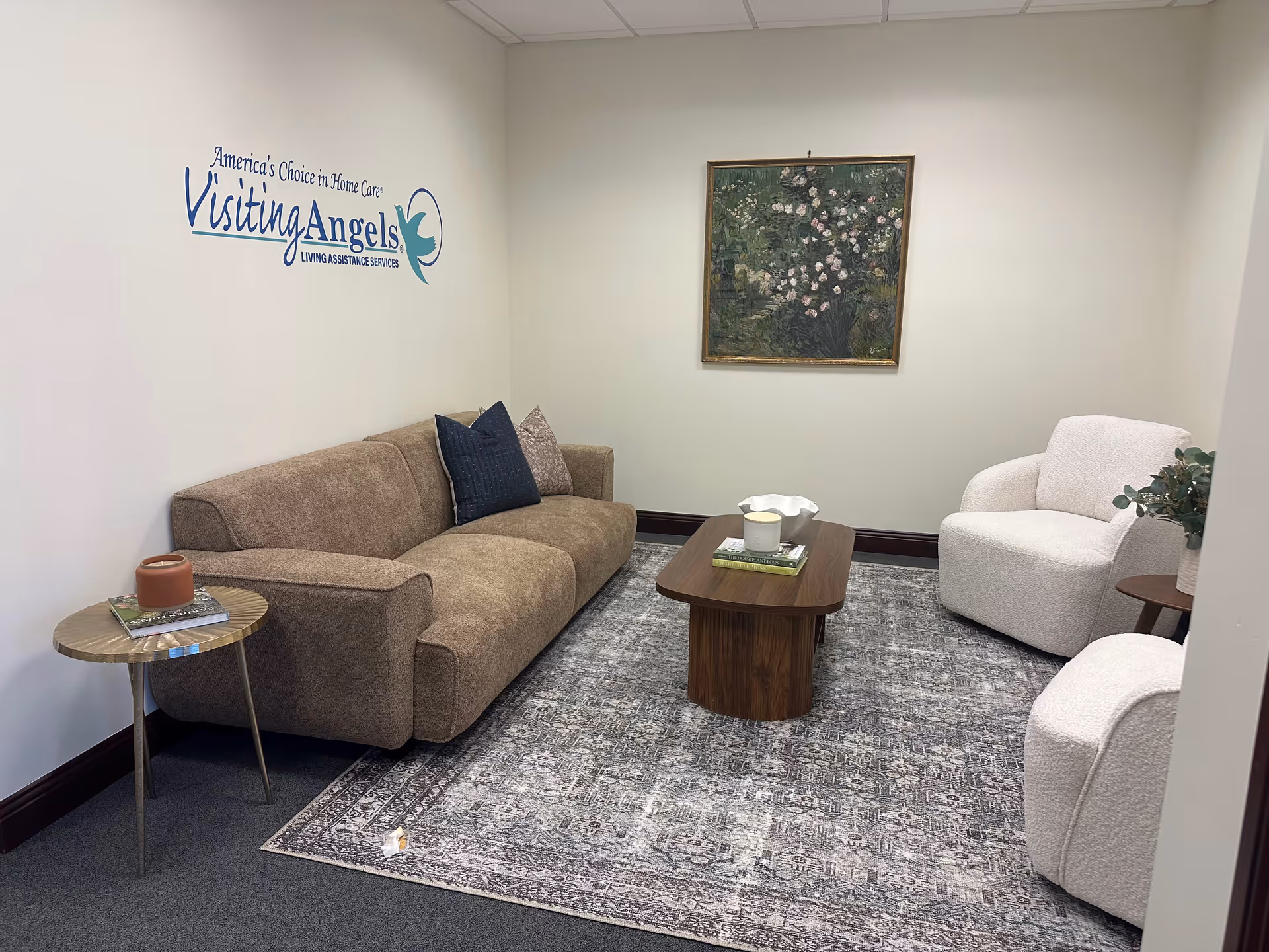 A waiting lounge with Visiting Angels logo, beige sofa, white chairs, and coffee table.