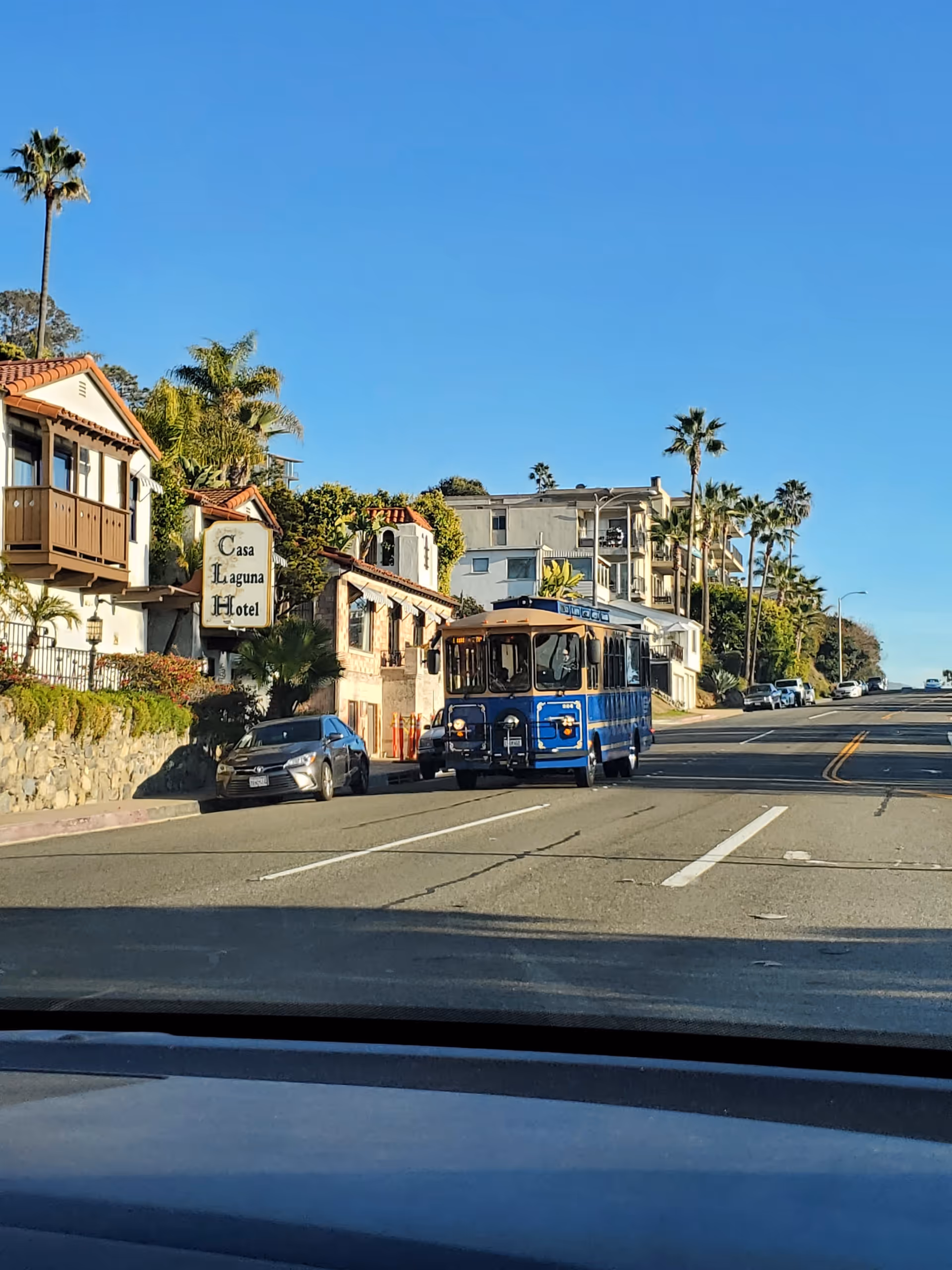 Blue trolley bus on a sunny coastal street beside hotel buildings.
