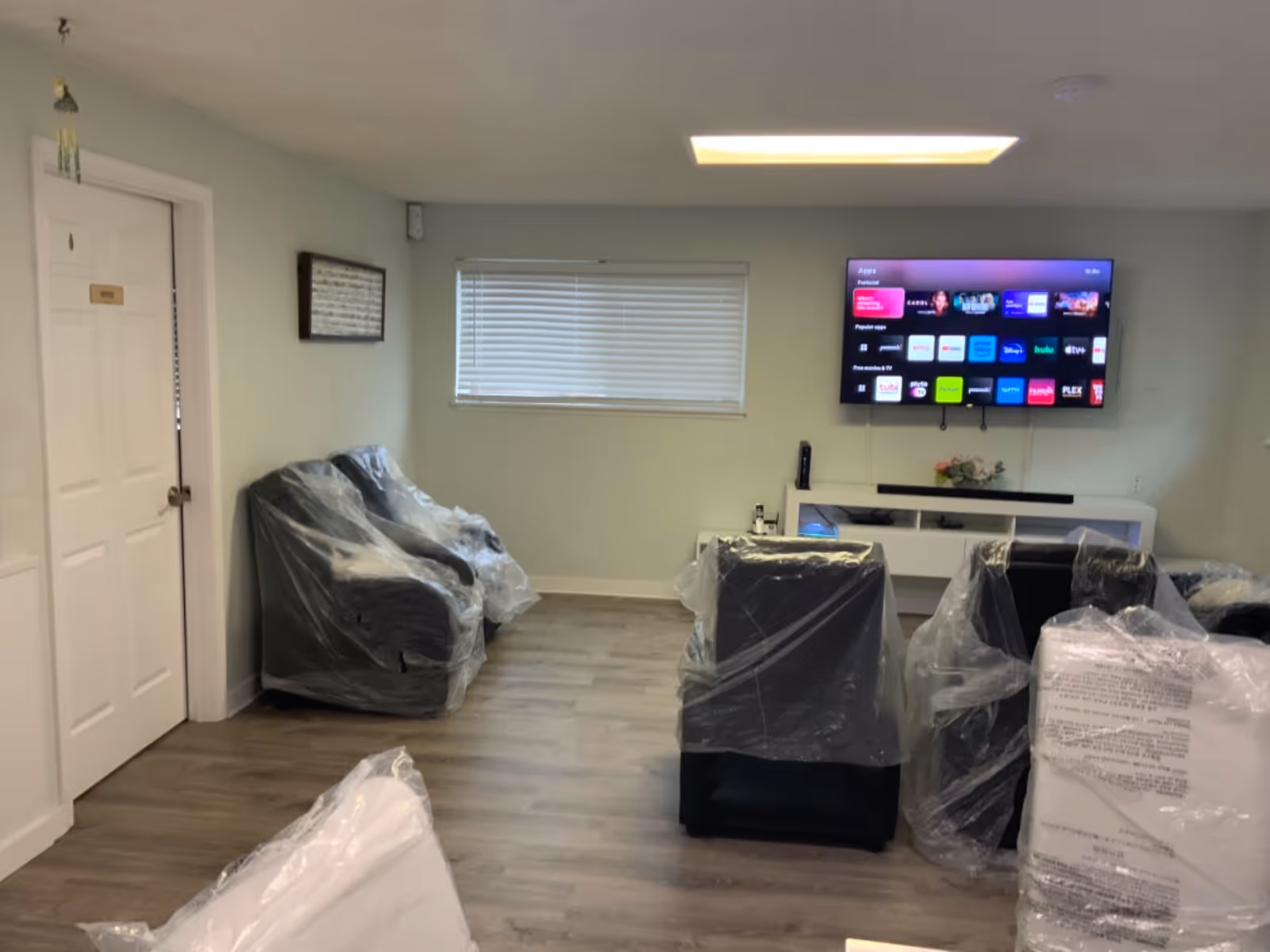 A furnished shared living room with plastic-covered chairs, a TV, and a white console.