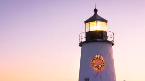 Sunset sky over a lighthouse with a wreath lit on its exterior wall.