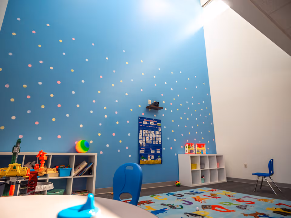 Bright blue wall with multicolored dots, toy shelves, and a colorful rug in a playroom.