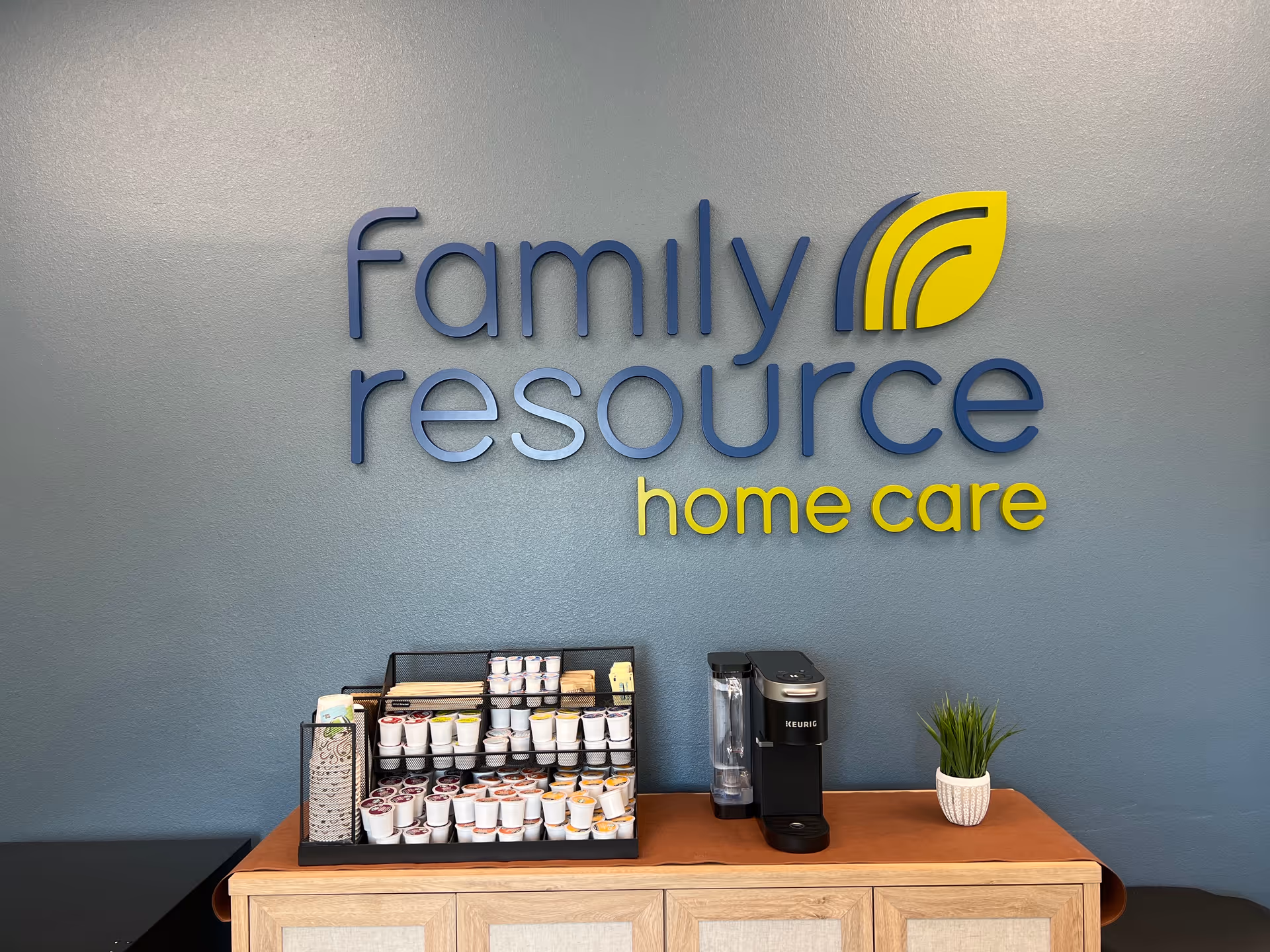 Reception area with blue wall, Family Resource Home Care logo, coffee station and plant.