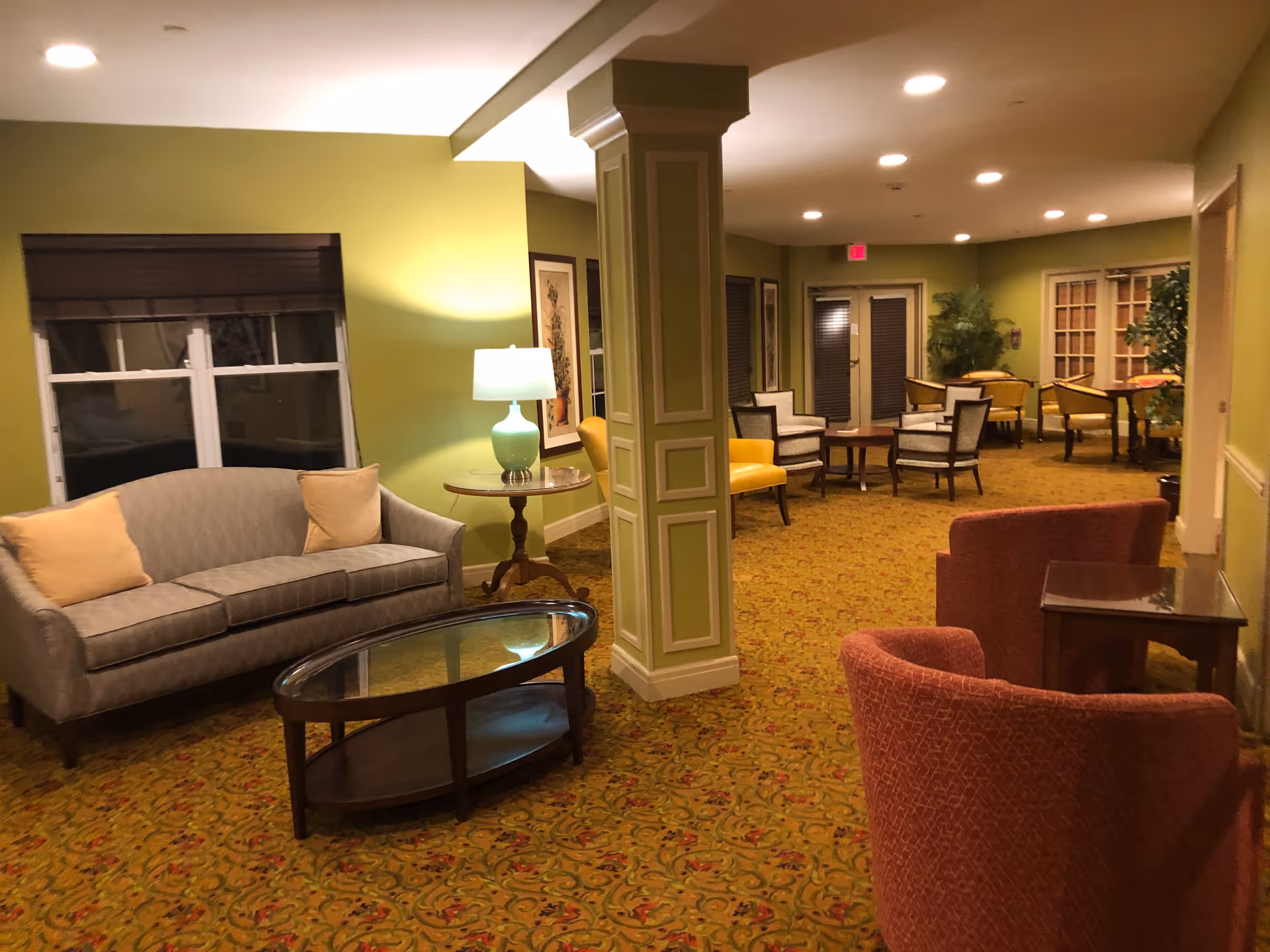 Colorful senior living lounge with green walls, sofas, chairs, and glass coffee tables.