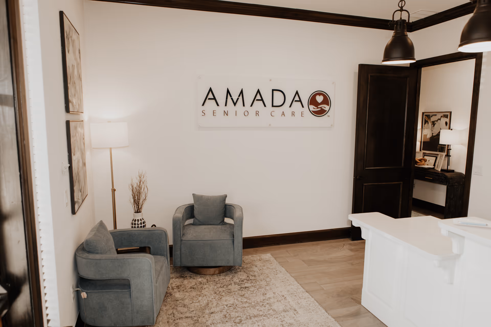 Lobby reception area with Amada Senior Care sign, seating, and a white reception desk.