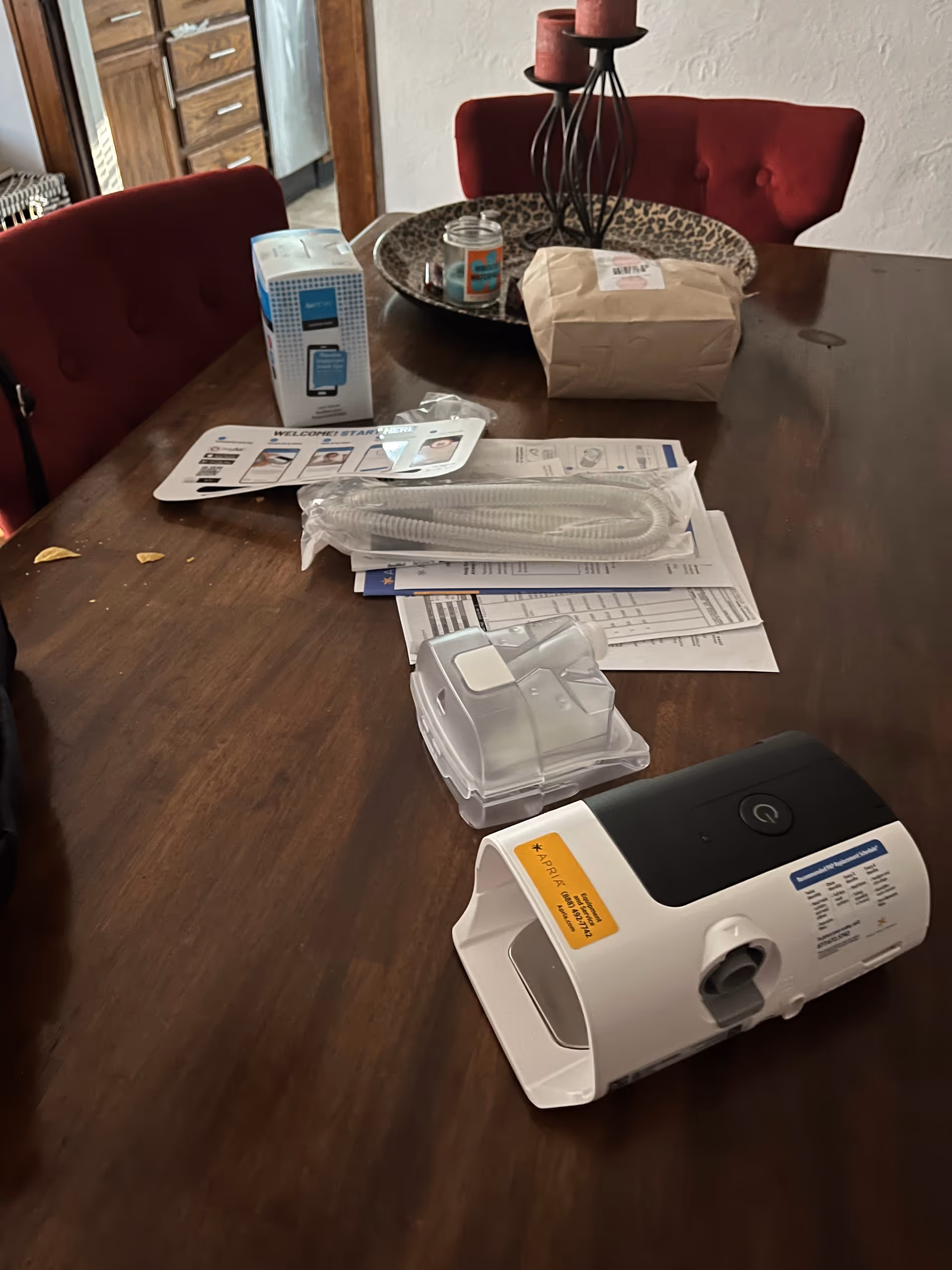 Apria healthcare medical device and paperwork on a dark wooden dining table in a dining room