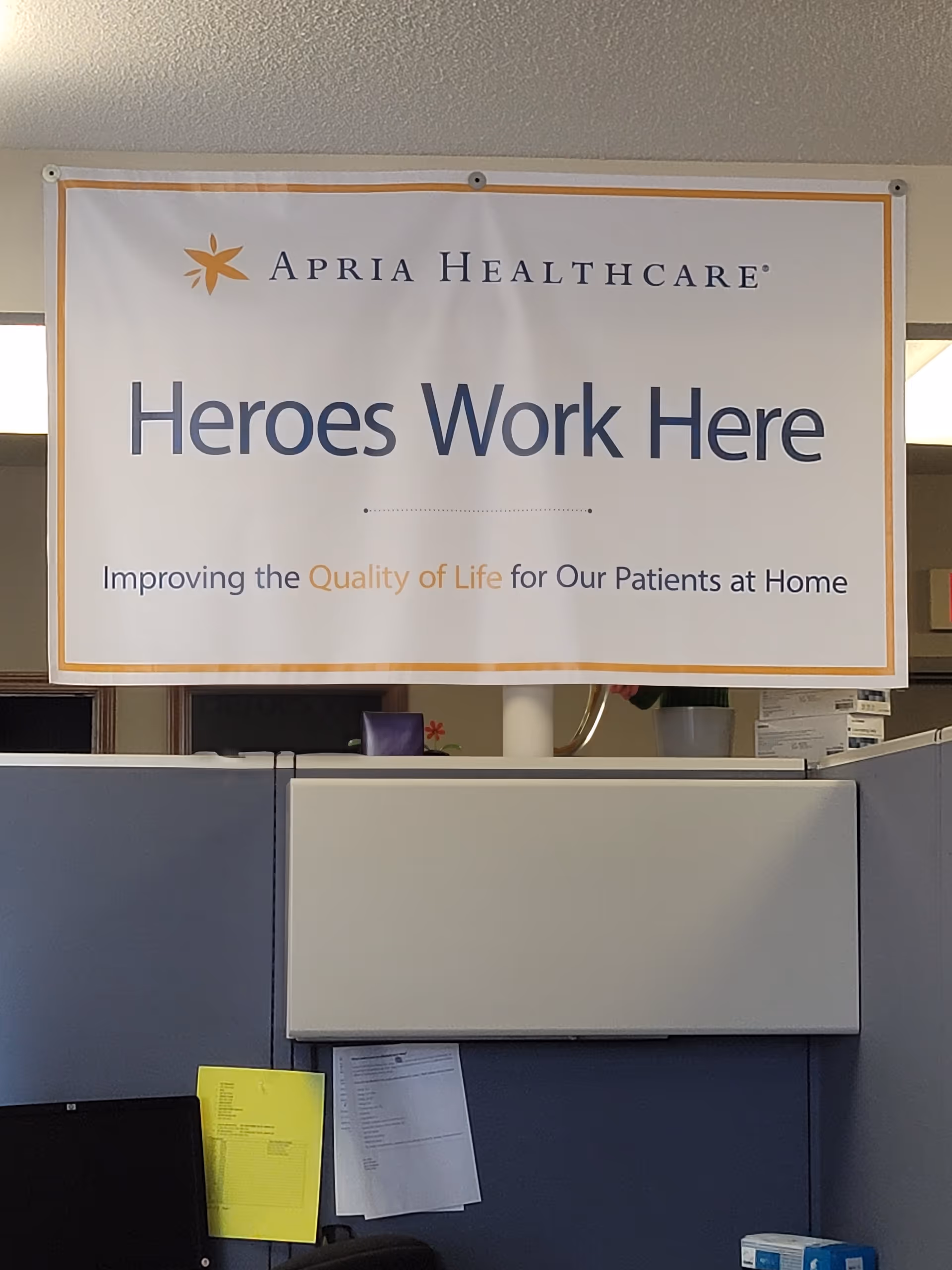 Apria Healthcare banner reading Heroes Work Here hung in an office cubicle area.