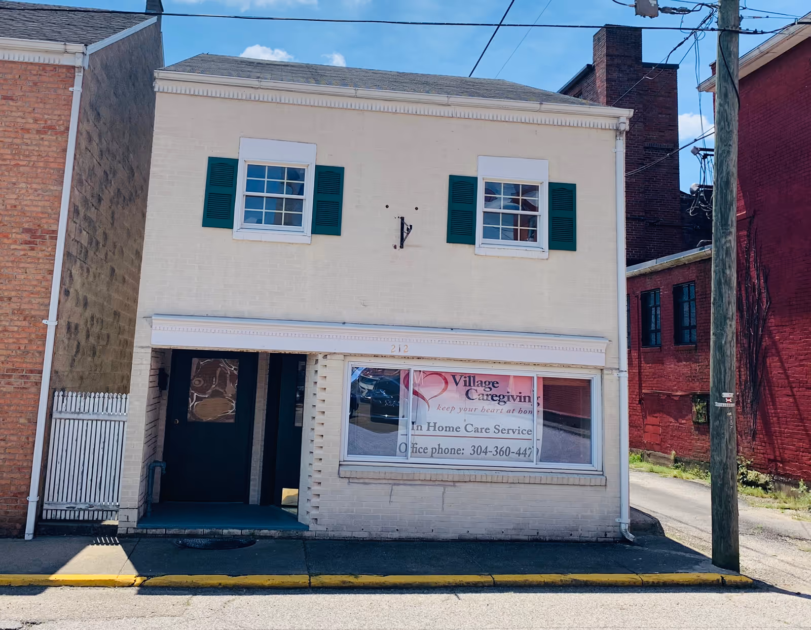 Two-story light brick building with Village Caregiving storefront and green shutters.