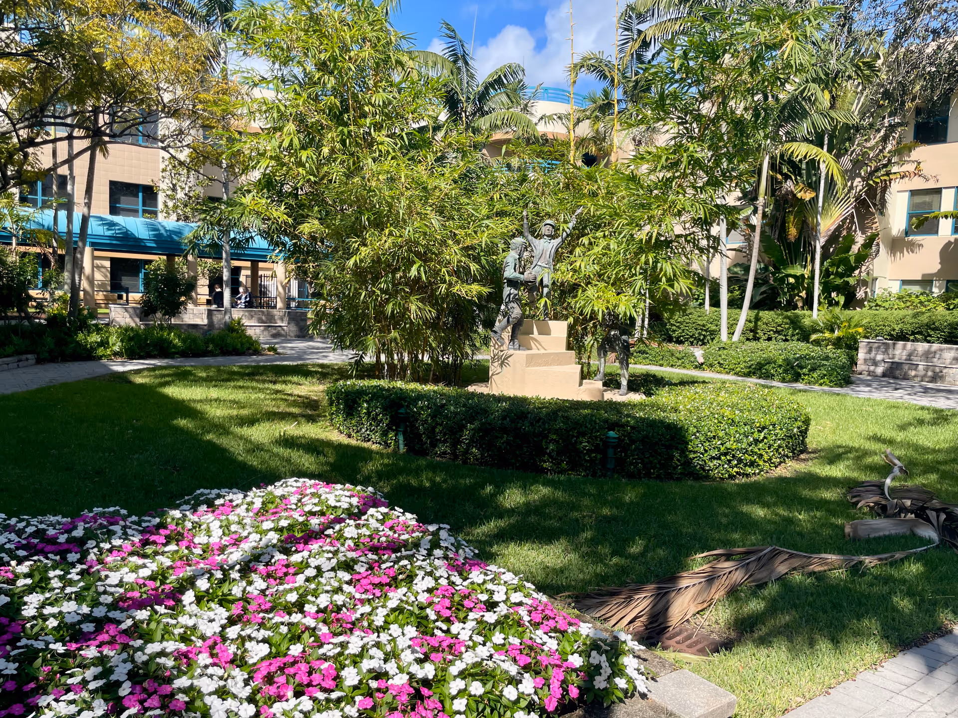 Outdoor courtyard of a senior living facility with a statue, greenery, and flowers.