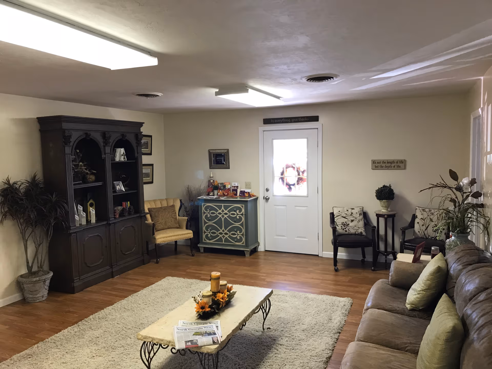 Cozy senior living common room with sofa, chairs, coffee table, and decorative cabinet.