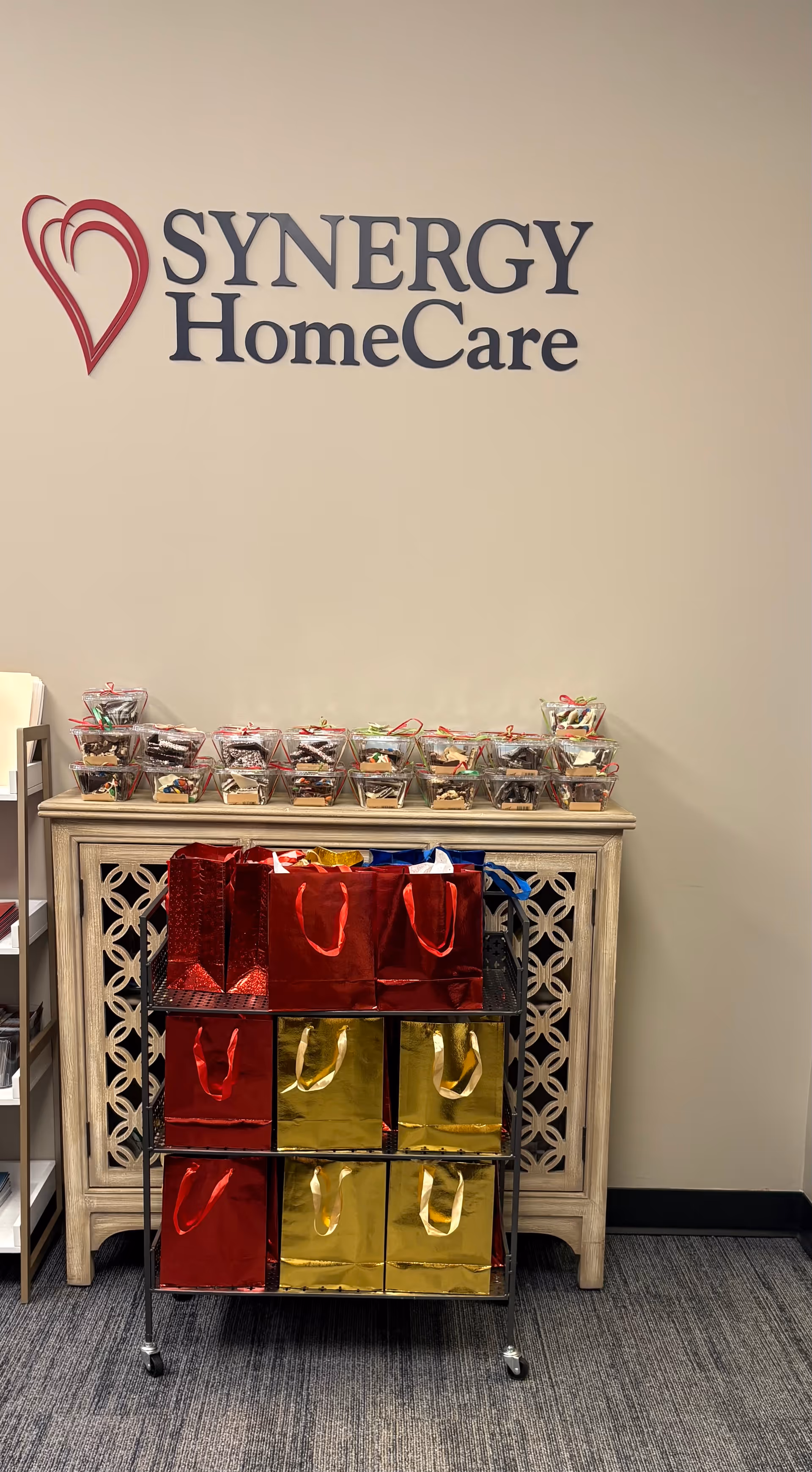 Interior scene featuring SYNERGY HomeCare logo with a cabinet and gift bags.