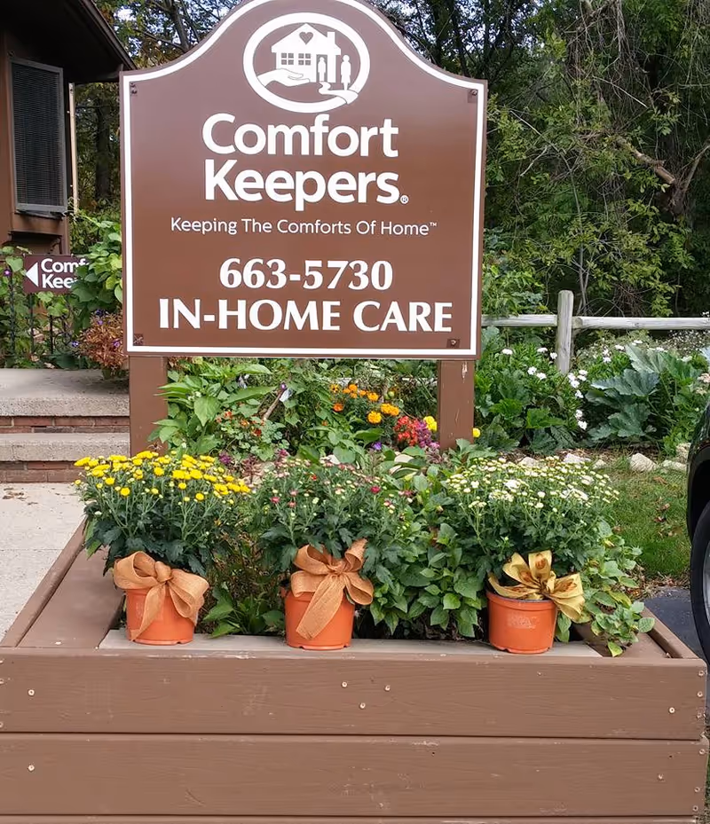 Brown Comfort Keepers sign with flower-filled planters in front of a facility